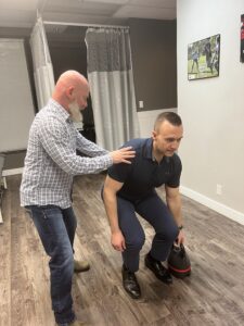 Man working with Physiotherapist to build core strength using kettle bell lifts during a physio-directed active rehab session.