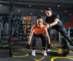 woman preparing to complete a deadlift while her trainer checks her form