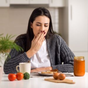 woman with nausea sitting a a table with uneaten food